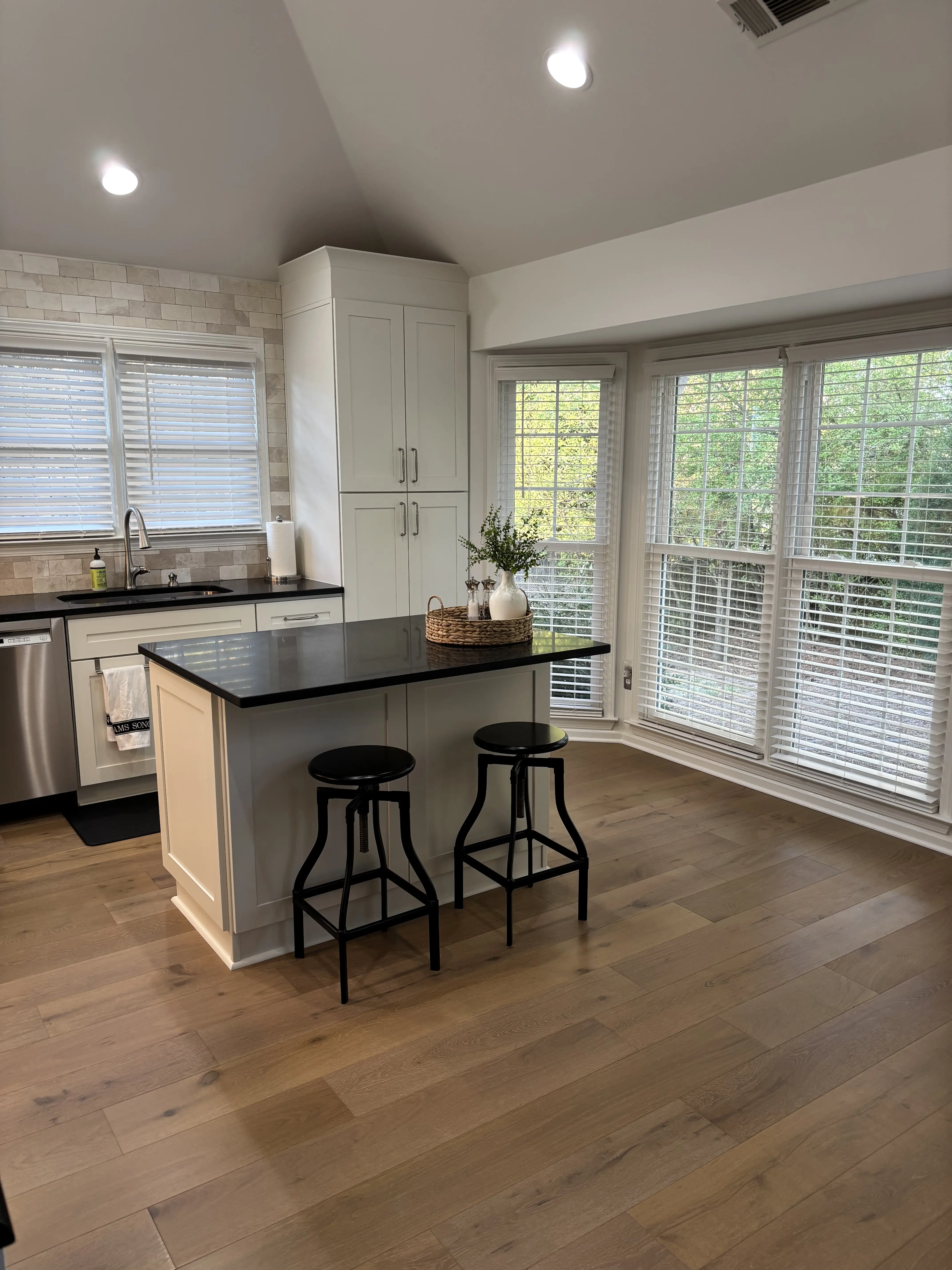 Kitchen renovation with a black-topped island, light shaker cabinets, stainless appliances, and a wall of windows at the breakfast nook.